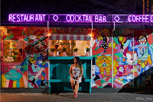 Smiling woman in colorful dress sitting in front of Sea Circus wearing Teva Sandals