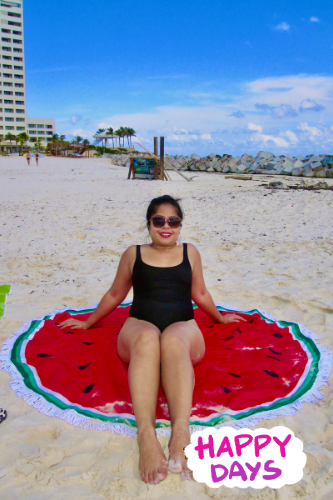 woman in black bathing suit sitting on watermelon print beach blanket